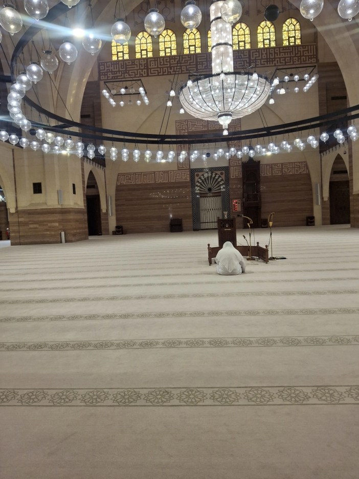 Man praying inside Al-Fateh Grand Mosque under chandelier – Islamic architecture in Bahrain with spiritual relevance to Sitra community