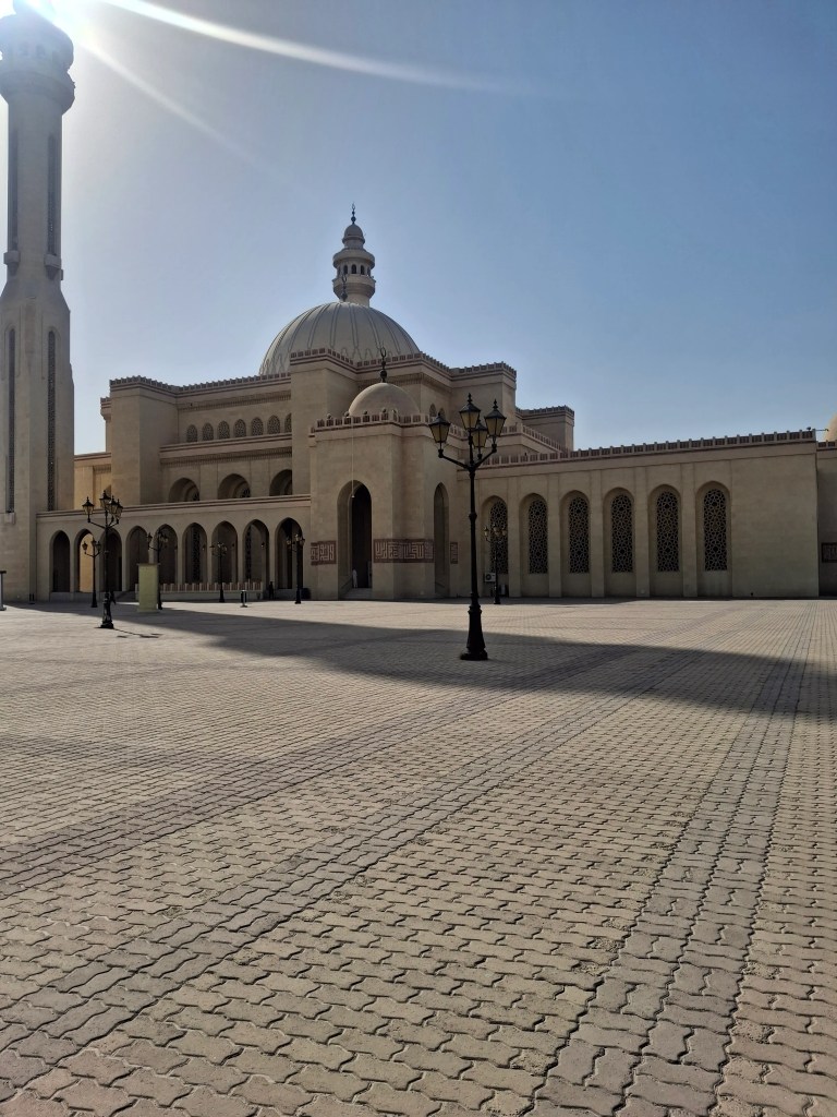"Exterior view of Al-Fateh Grand Mosque in Manama, Bahrain, under bright morning sunlight with minaret and large dome architecture"

