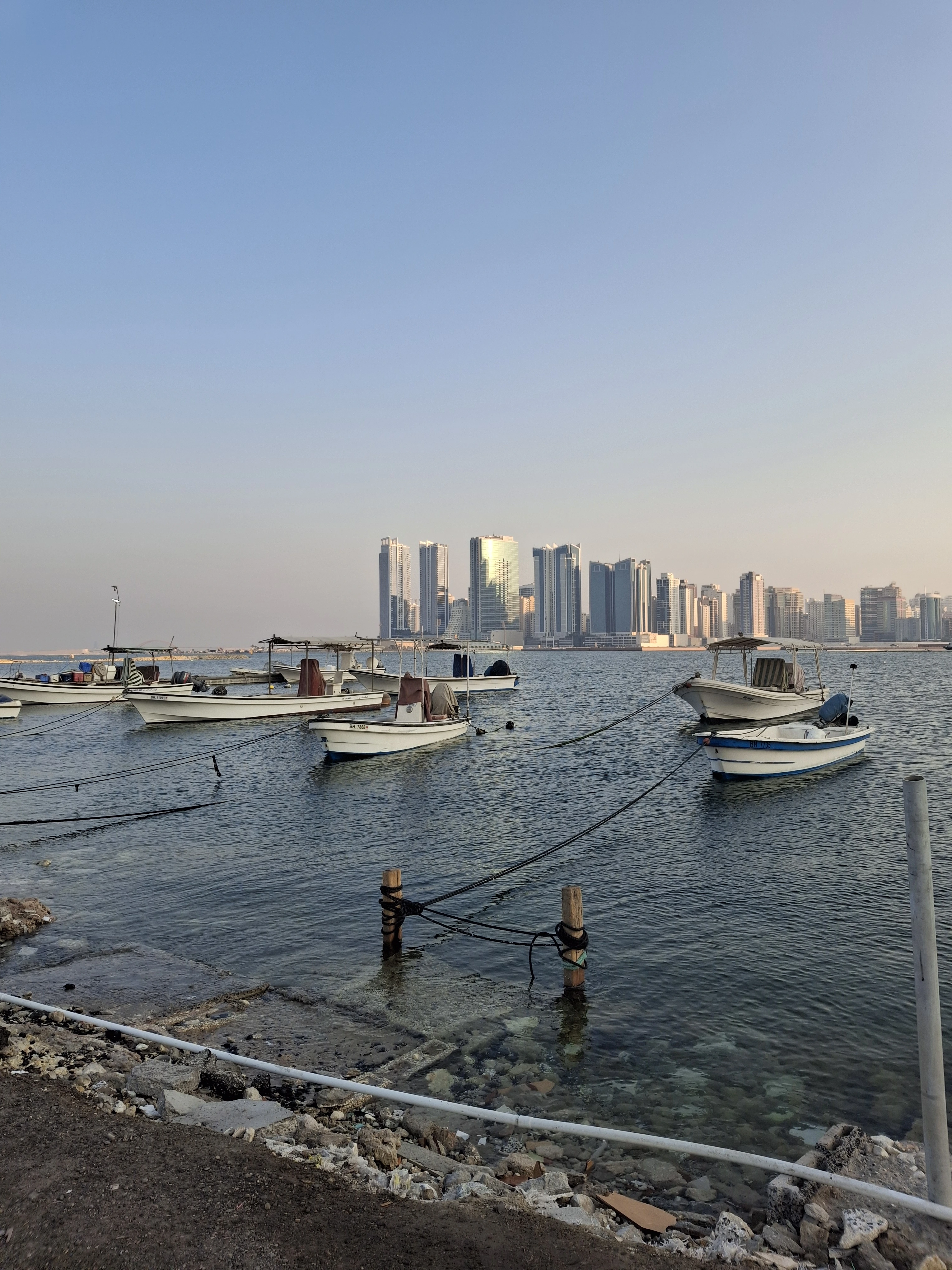 “Small fishing boats anchored at Bahrain Marina with the modern Manama skyline in the background during sunset.”