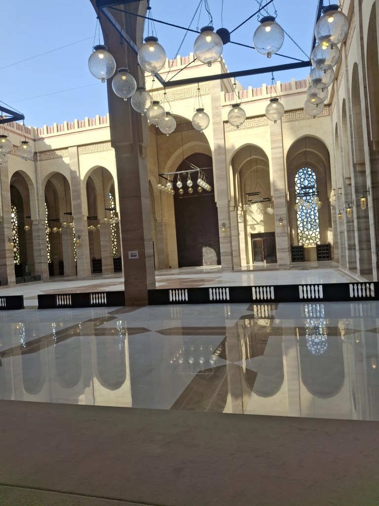Interior of Al-Fateh Grand Mosque in Bahrain featuring Islamic calligraphy, large chandelier, and ornate architectural design