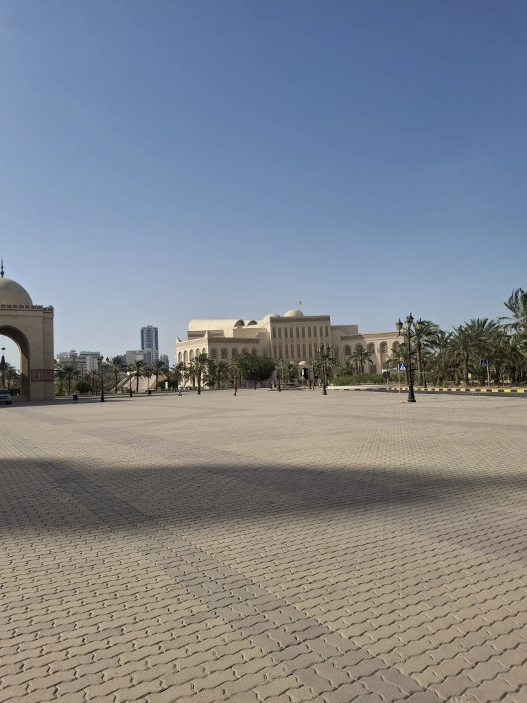 "Side view of Al-Fateh Grand Mosque in Bahrain with visible dome, minaret, and courtyard arches under clear blue sky."