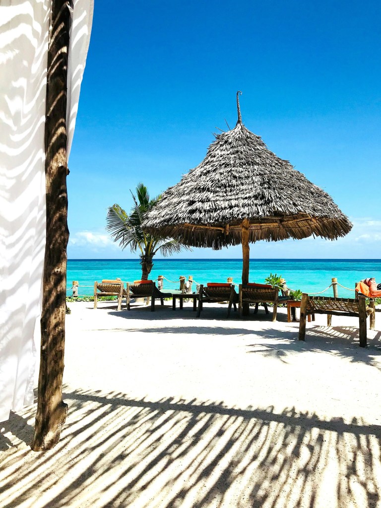 Thatched straw umbrella and lounge chairs on a sandy Zanzibar beach under clear blue skies
