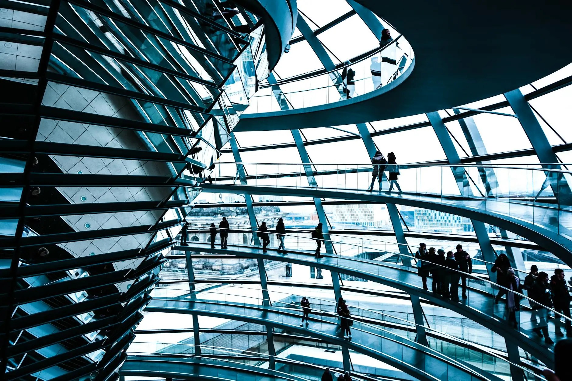 Interior view of the glass dome of the Reichstag building in Berlin, showcasing its spiral structure and visitors strolling on the viewing platforms.