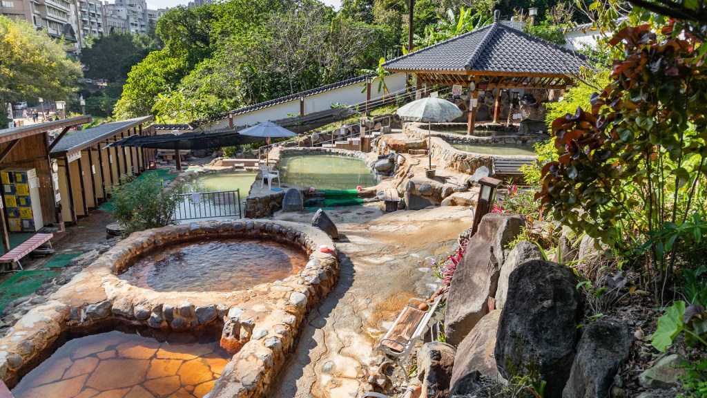 A serene view of natural hot springs surrounded by lush greenery and traditional architecture in Beitou, Taipei.