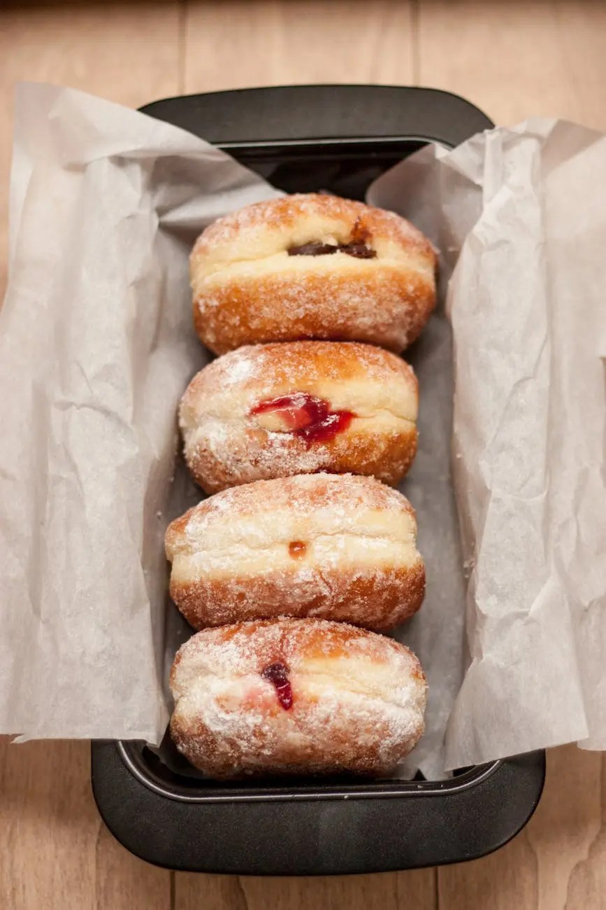 A tray filled with dusted Berliner Pfannkuchen (jam-filled donuts) placed on parchment paper.