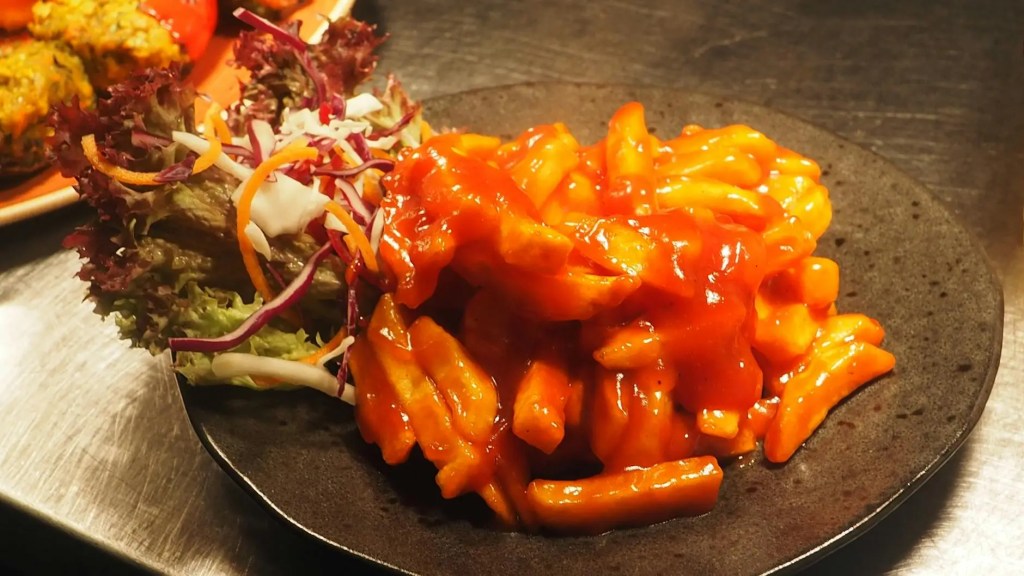 A plate of spicy tteokbokki, a popular Korean street food made from chewy rice cakes in a red, spicy sauce, served with a side of fresh salad.