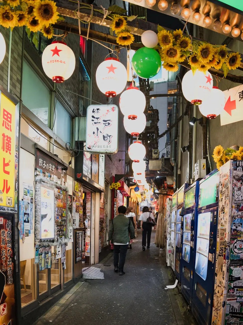 Narrow alleyway in Osaka adorned with lanterns and sunflower decorations, bustling with pedestrians and lively storefronts.