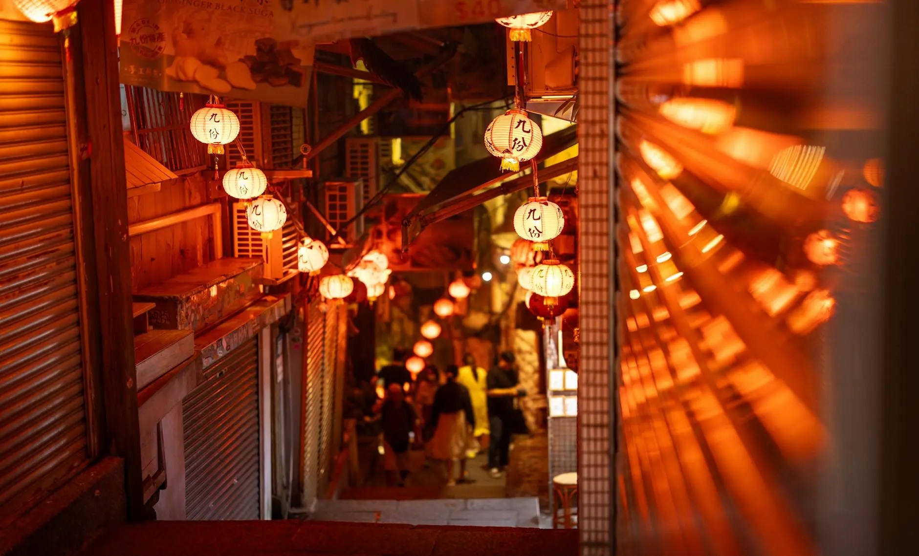 A narrow alleyway illuminated by traditional Chinese lanterns, giving a warm orange glow, with people walking in the distance.