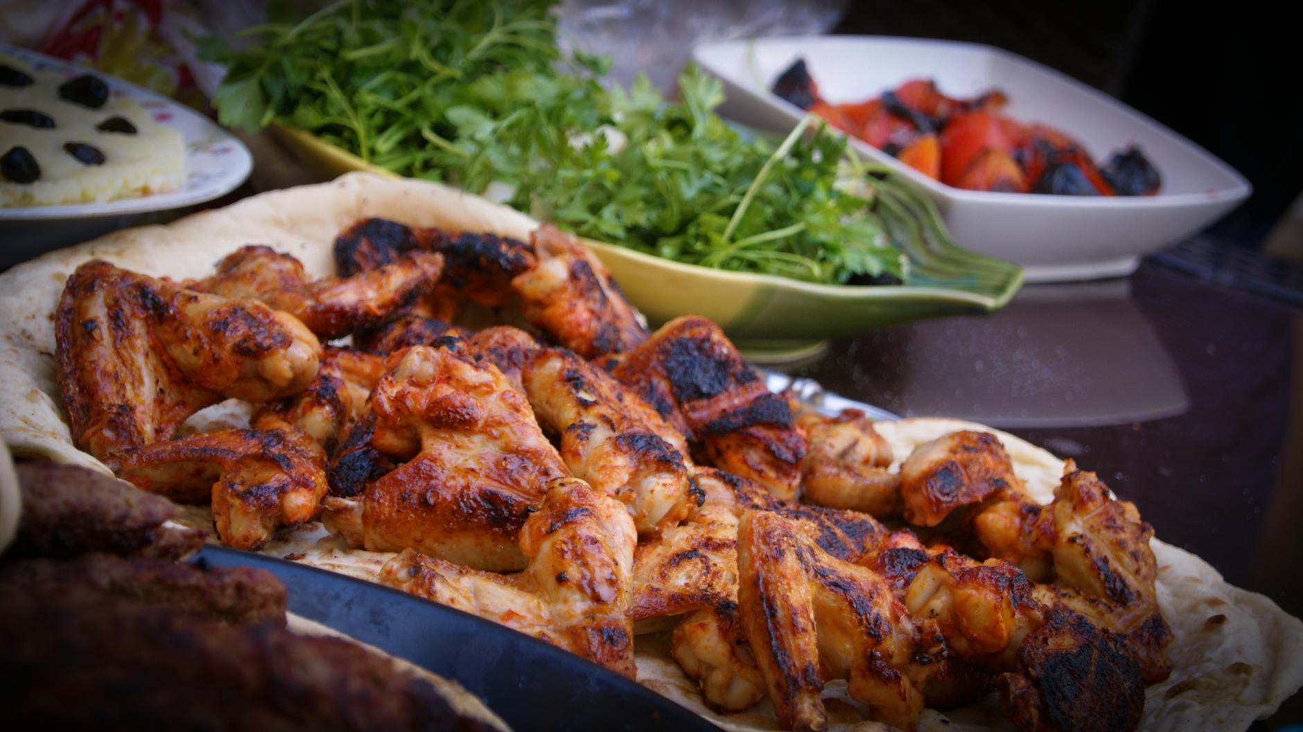 Platter of grilled chicken wings served on flatbread, garnished with fresh herbs and accompanied by a side of assorted vegetables.