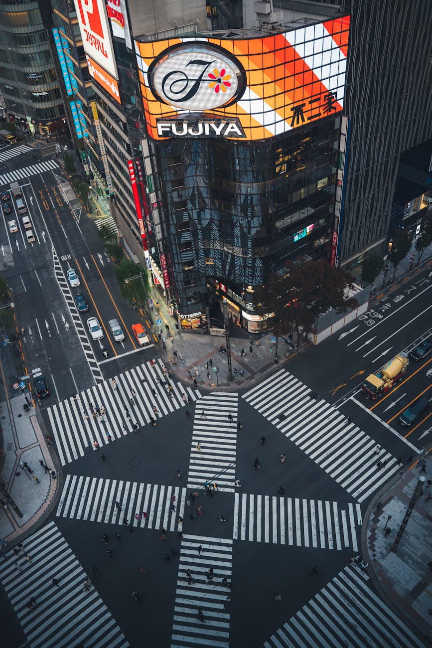 Aerial view of Shibuya Crossing in Tokyo, showcasing busy pedestrian pathways and bustling streets, with bright advertisements on surrounding buildings.