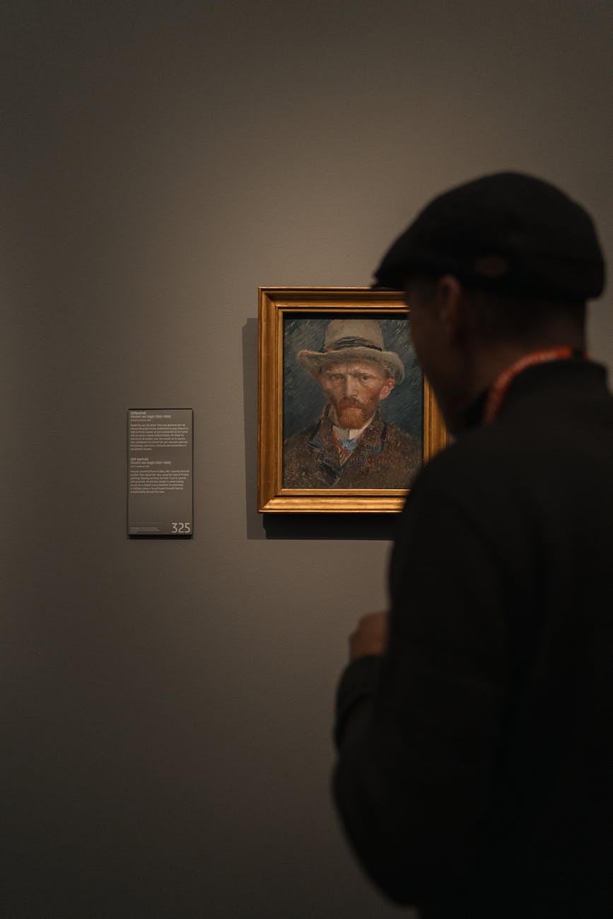 A visitor standing in front of a framed portrait of Vincent van Gogh in a museum, with a wall plaque displaying information about the artwork.