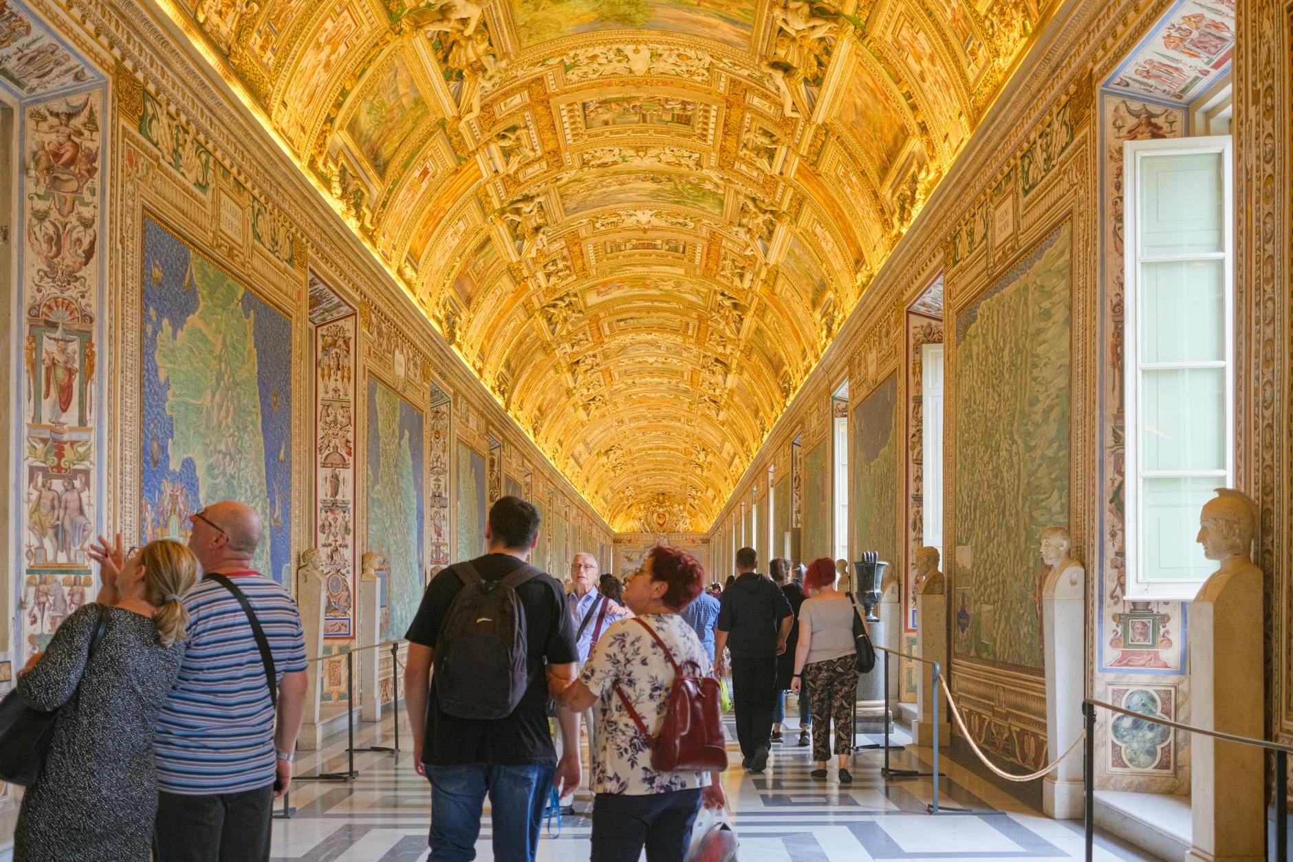 Visitors exploring the ornate Vatican Museums, admiring the intricately decorated walls and golden ceilings.