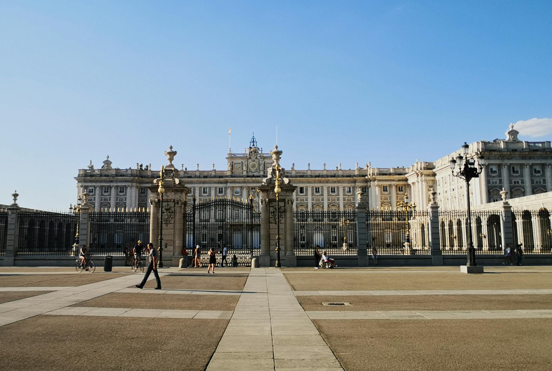 View of the Royal Palace of Madrid, showcasing its grand architecture and surrounding gardens on a clear blue sky day.