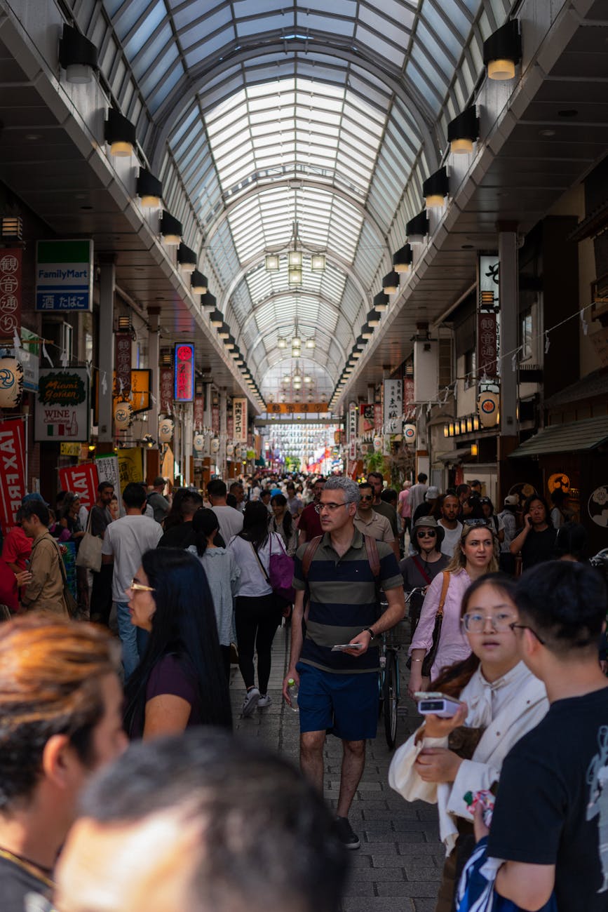A bustling shopping street in Tokyo filled with people, lined with colorful storefronts and hanging lanterns.