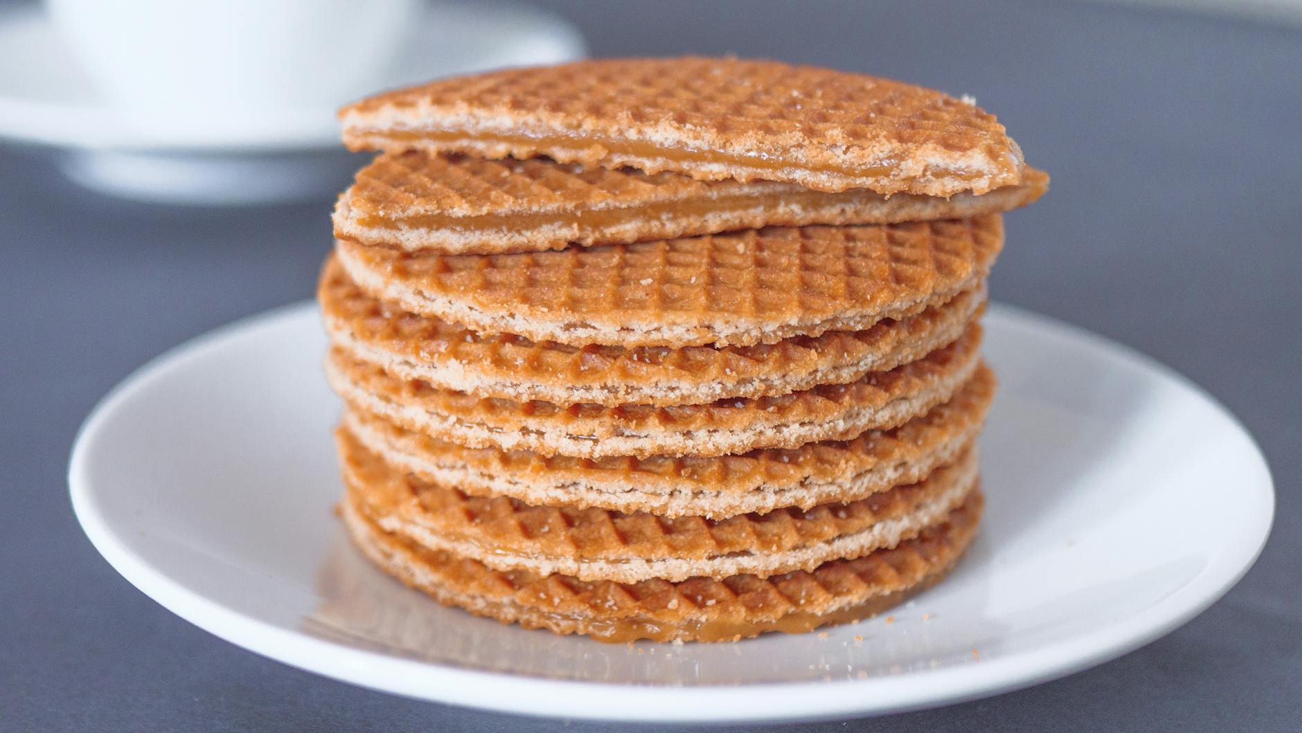 A stack of golden-brown stroopwafels on a white plate, with a blurred cup in the background.