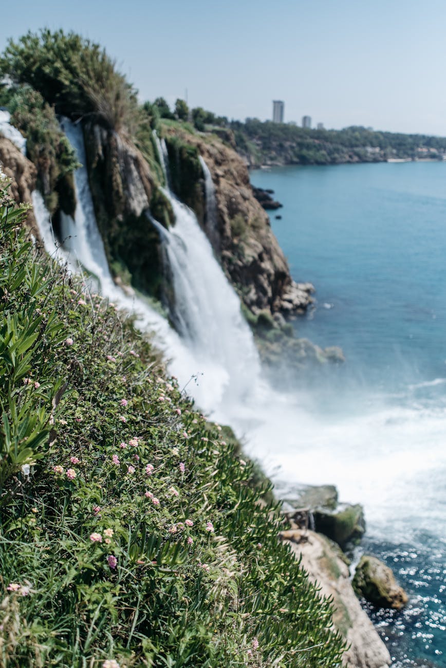 "Düden Waterfalls – Nature’s Spectacle Where River Meets the Sea" A scenic view of Düden Waterfalls cascading into the Mediterranean Sea, surrounded by lush greenery and rocky cliffs.