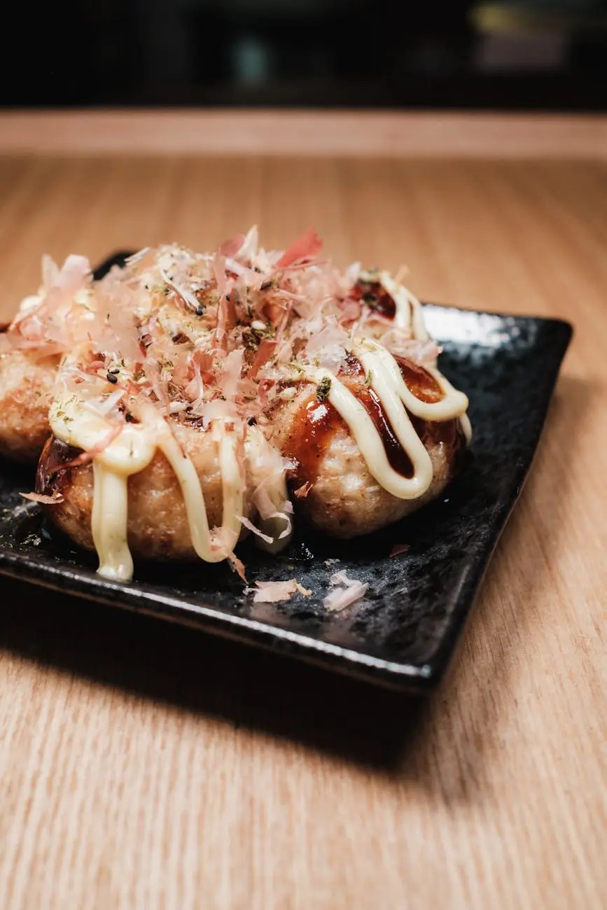 A close-up of a plate of takoyaki, octopus balls, drizzled with mayonnaise and topped with bonito flakes and green seasoning.