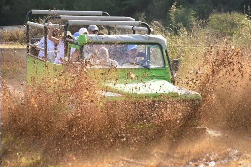 An off-road vehicle splashes through muddy terrain during an adventure tour, with passengers enjoying the ride.