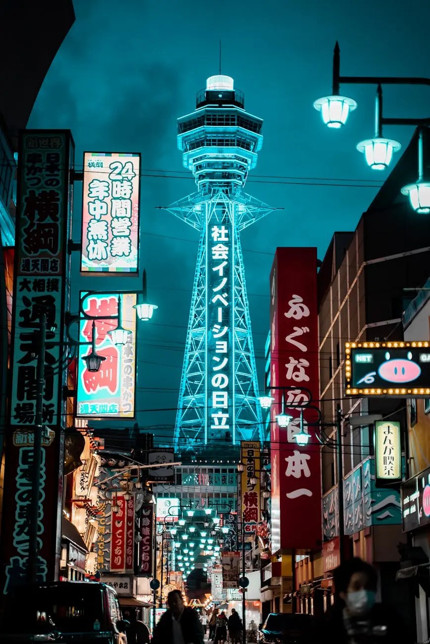 Night view of Tsutenkaku Tower illuminated in blue, surrounded by colorful neon signs and bustling streets in Osaka.