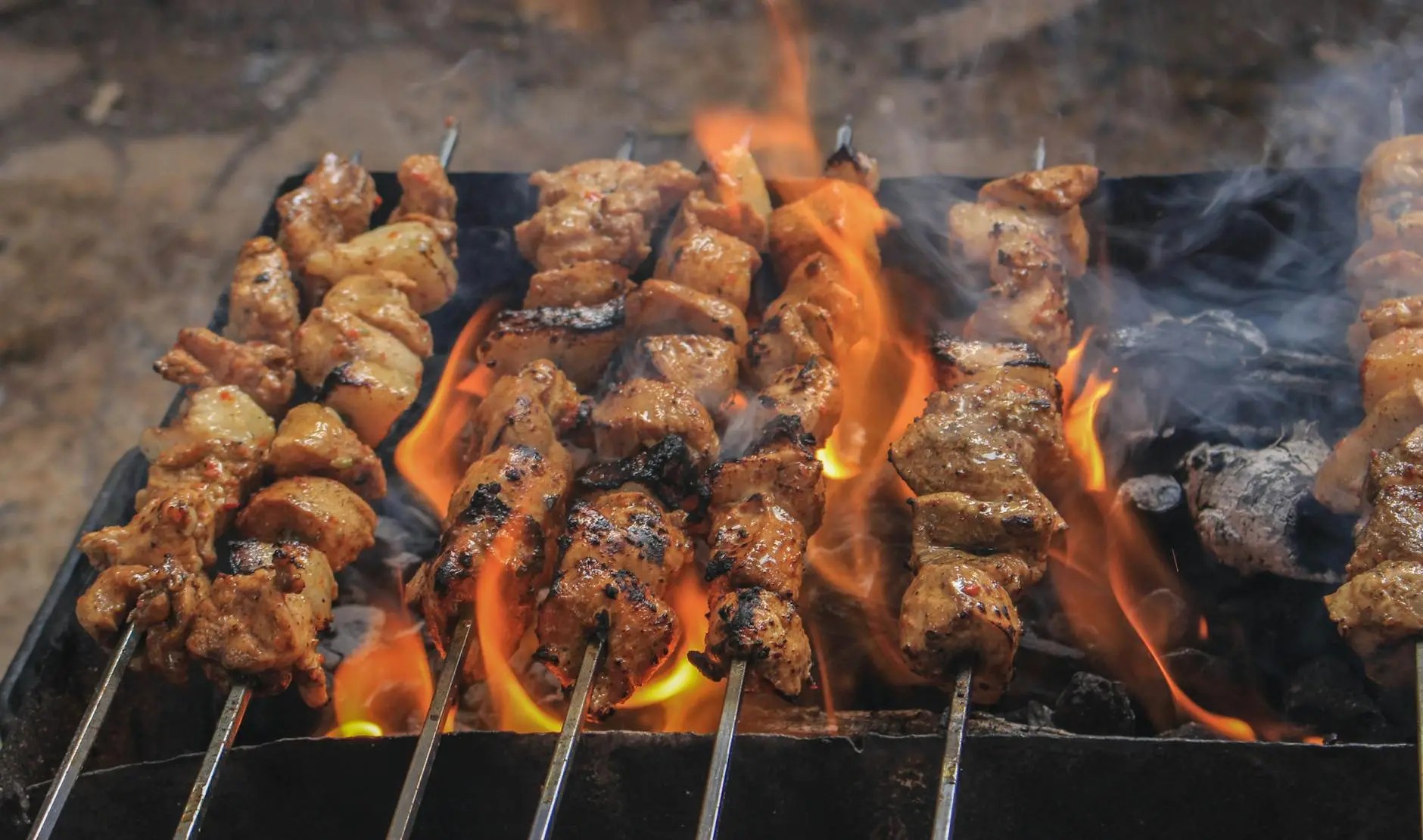 Grilled meat skewers over an open flame with smoke rising, showcasing a delicious barbecue cooking process.