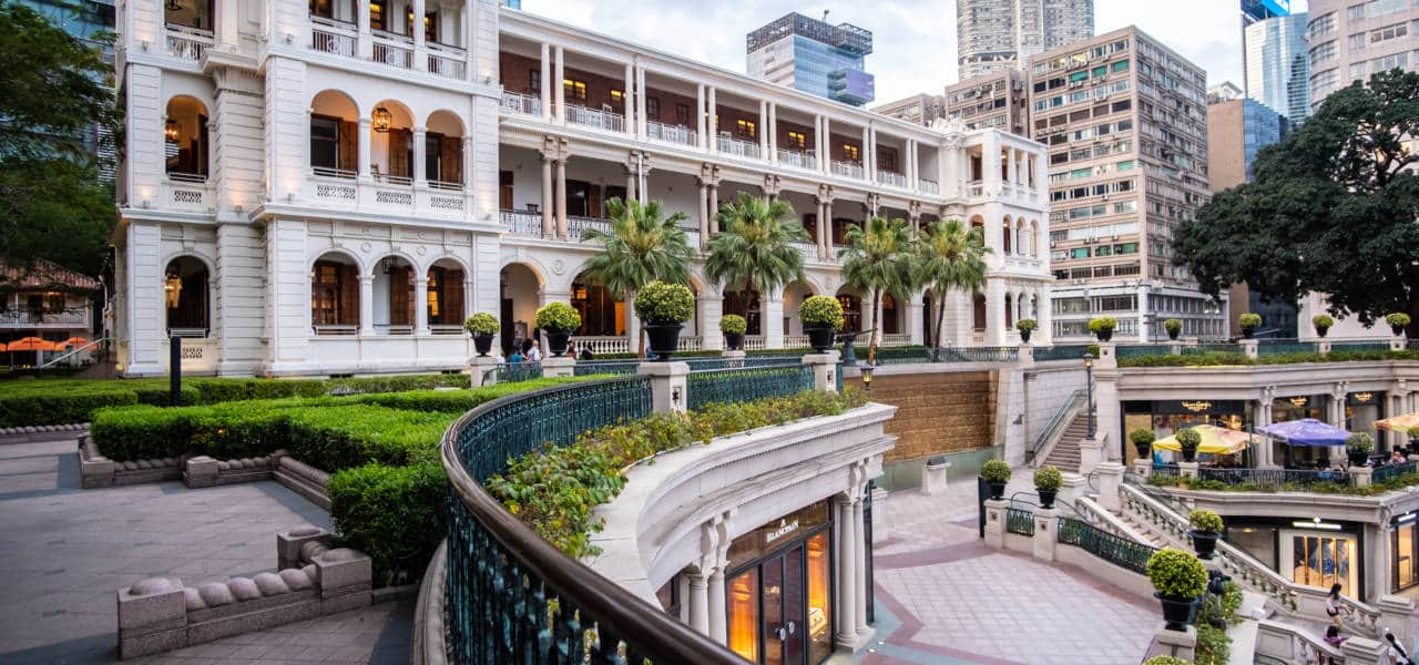 A beautifully restored heritage building in Hong Kong, featuring classic European architectural details, surrounded by lush greenery and modern skyscrapers in the background.