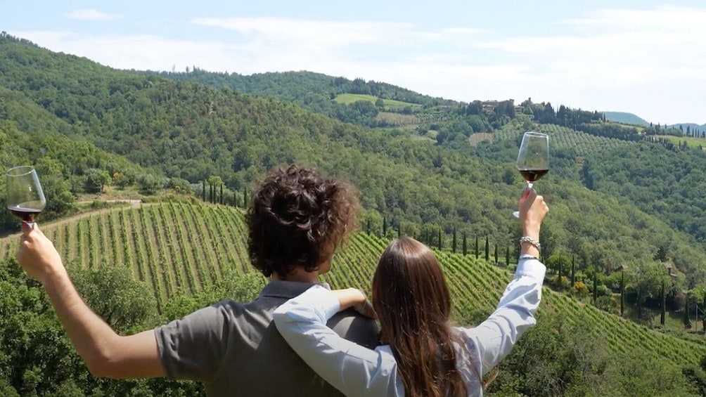 A couple enjoying wine with a scenic view of rolling vineyards in Tuscany, Italy.