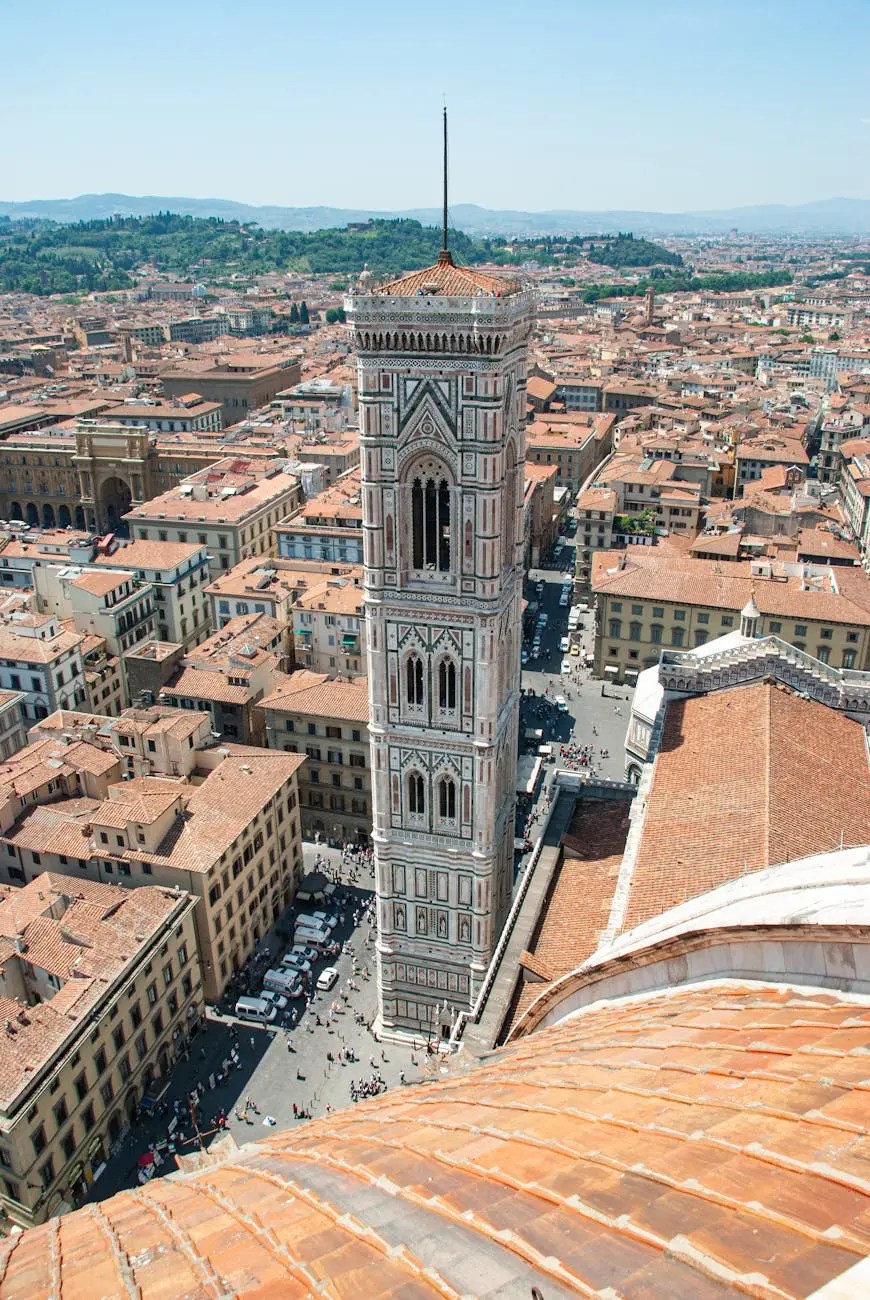 Aerial view of Florence with the Giotto's Campanile tower prominently featured, surrounded by terracotta rooftops and distant hills under a clear blue sky.