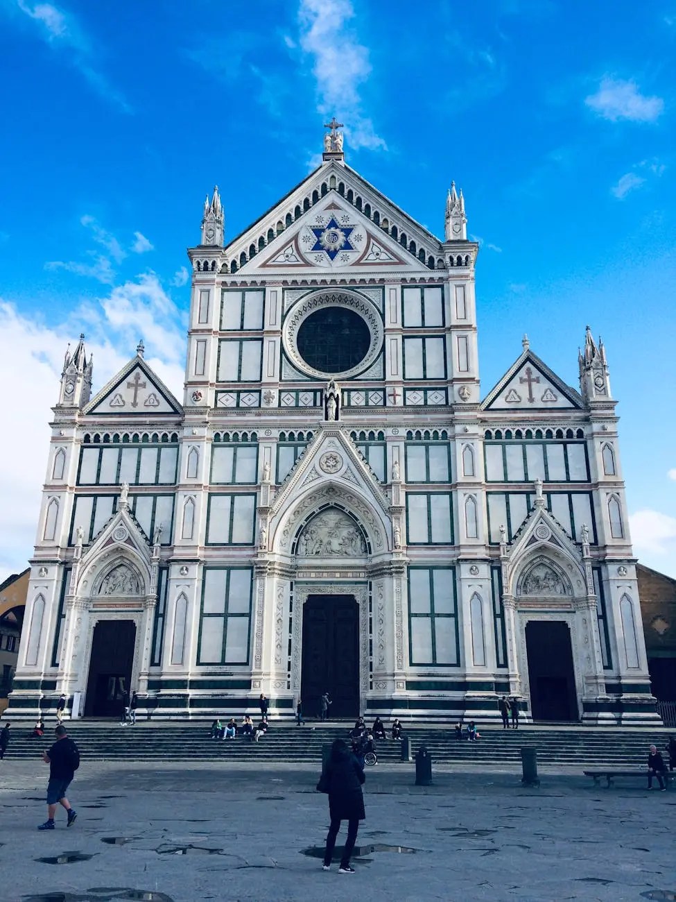 Facade of the Basilica of Santa Croce in Florence, Italy, showcasing intricate architecture and detailed stonework against a clear blue sky.