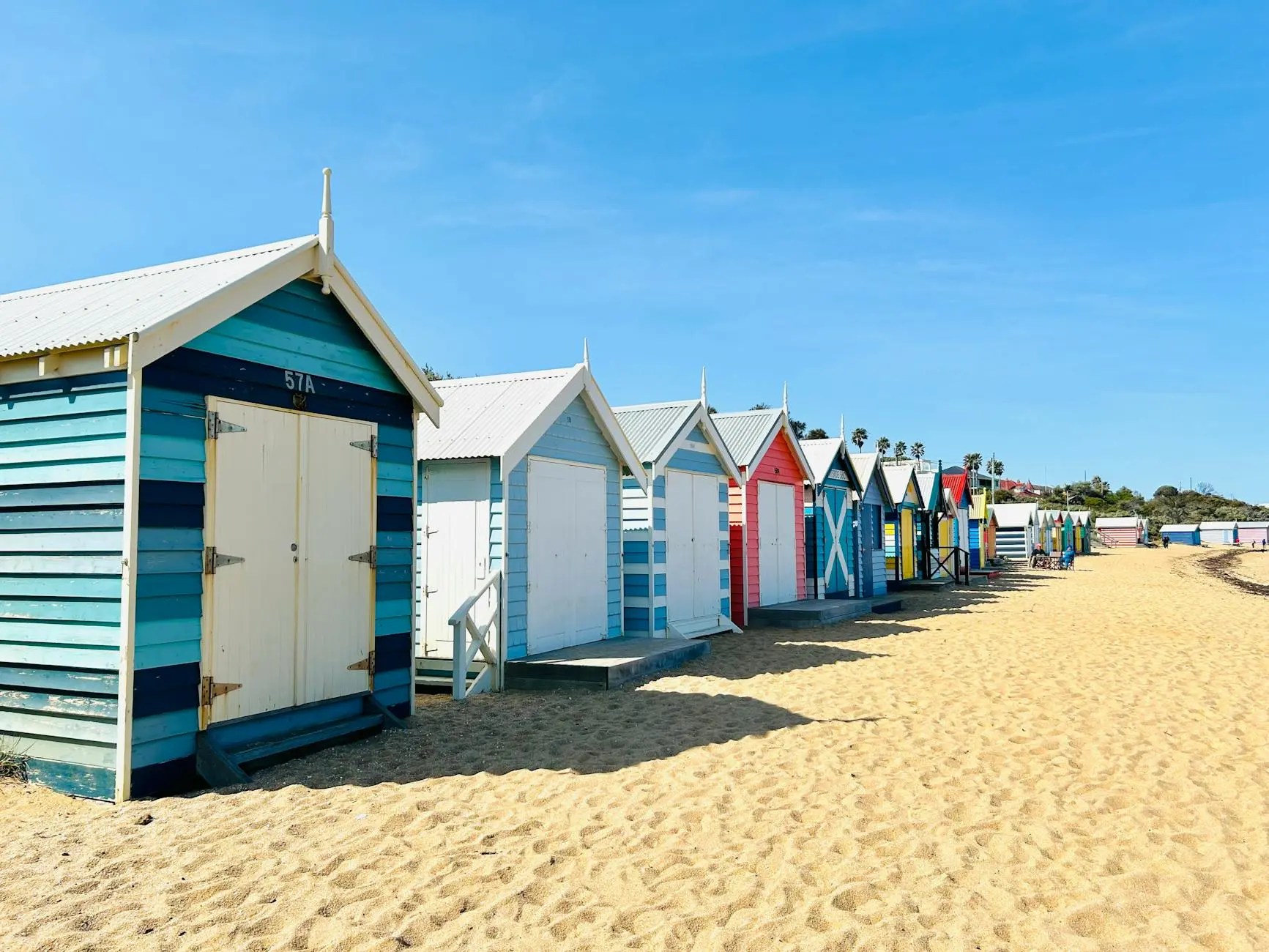 Colorful beach huts lined up along a sandy beach under a clear blue sky.