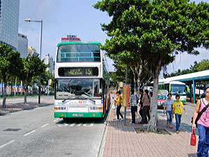A city bus in Hong Kong showing the route number 15, with passengers waiting nearby on a sunny day.