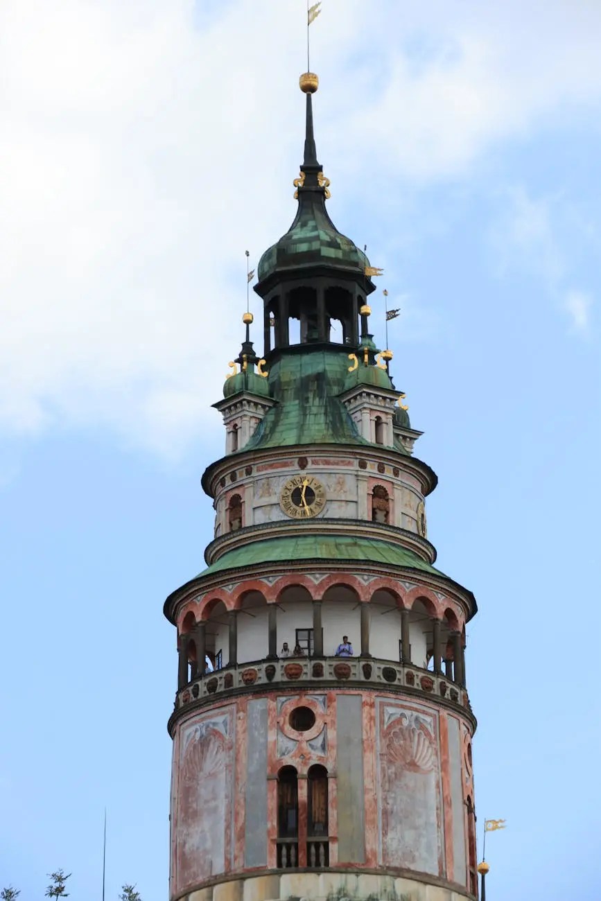 Close-up of a historic tower with a green dome, decorative details, and a clock, set against a blue sky.