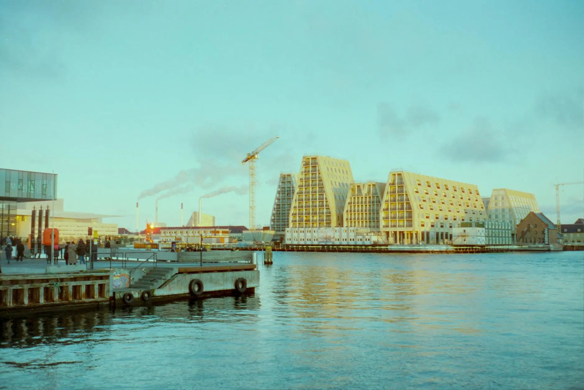 A scenic view of modern architecture along a waterfront in Copenhagen, featuring unique building designs with a backdrop of a clear sky.