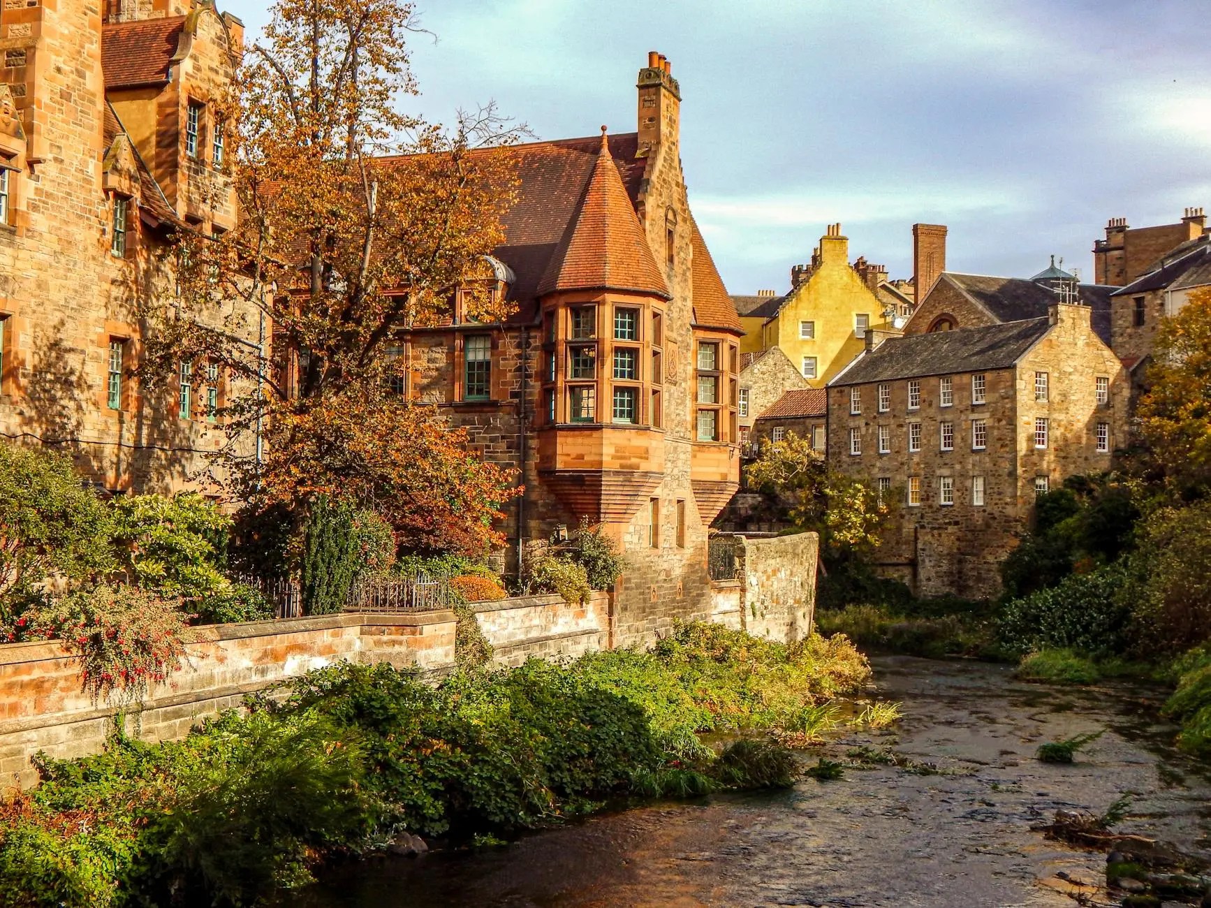 A scenic view of charming historic buildings along a riverbank in Edinburgh, Scotland, with autumn foliage and a tranquil atmosphere.