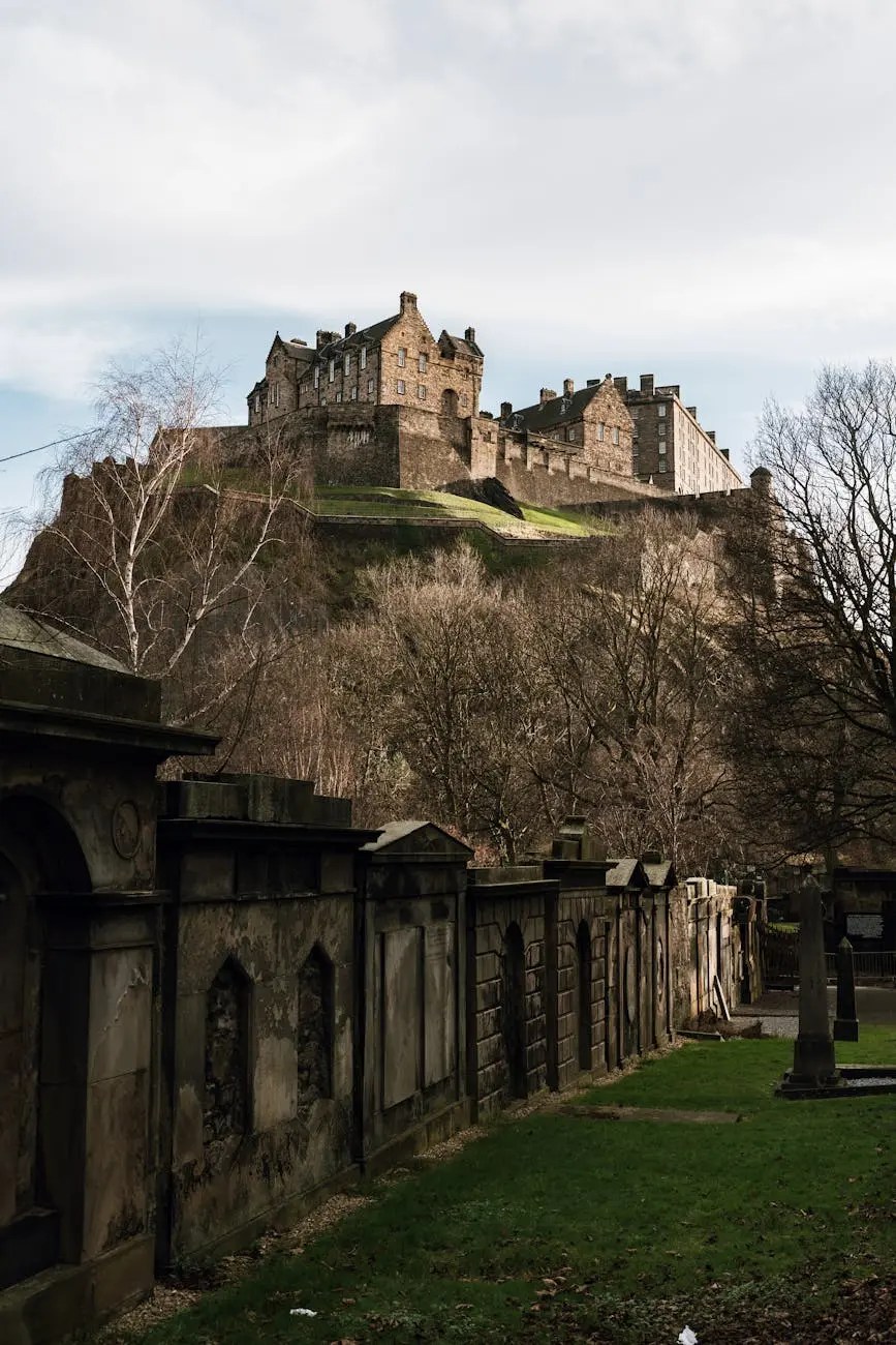 View of Edinburgh Castle perched atop a rocky hill, surrounded by bare trees and an overcast sky.