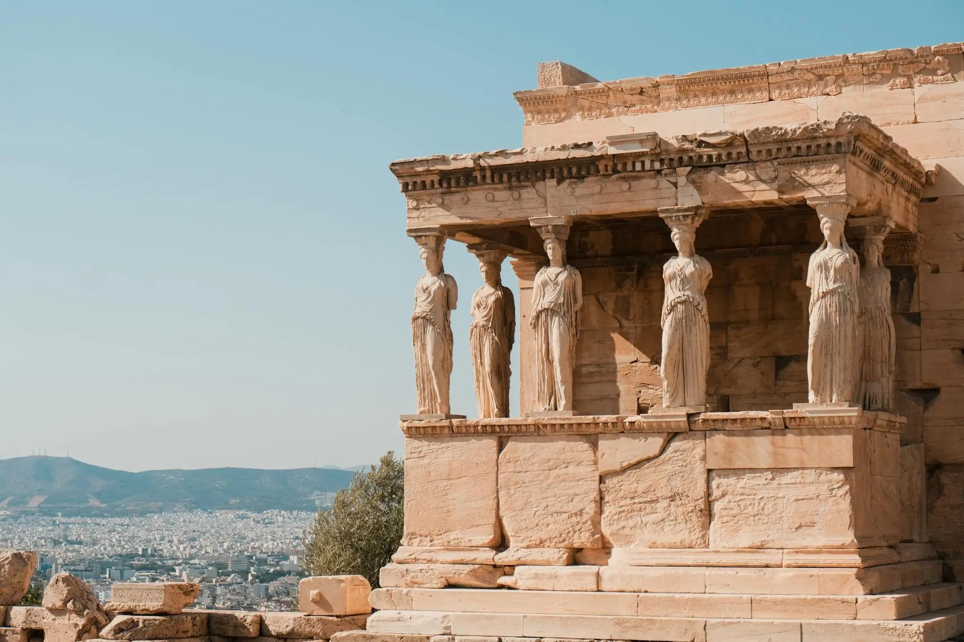 View of the Erechtheion temple on the Acropolis in Athens, Greece, showcasing its iconic Caryatids and ancient architectural features against a clear blue sky.