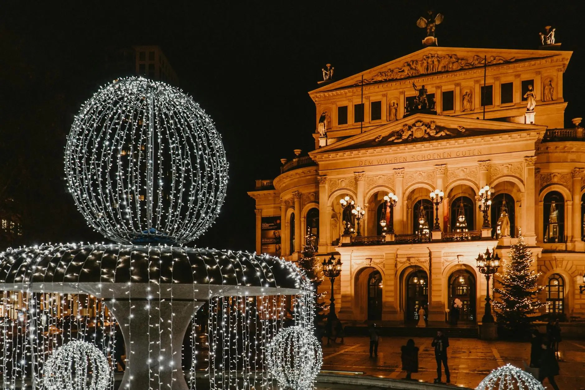 A beautifully illuminated fountain adorned with lights in front of the Alte Oper (Old Opera House) in Frankfurt at night.