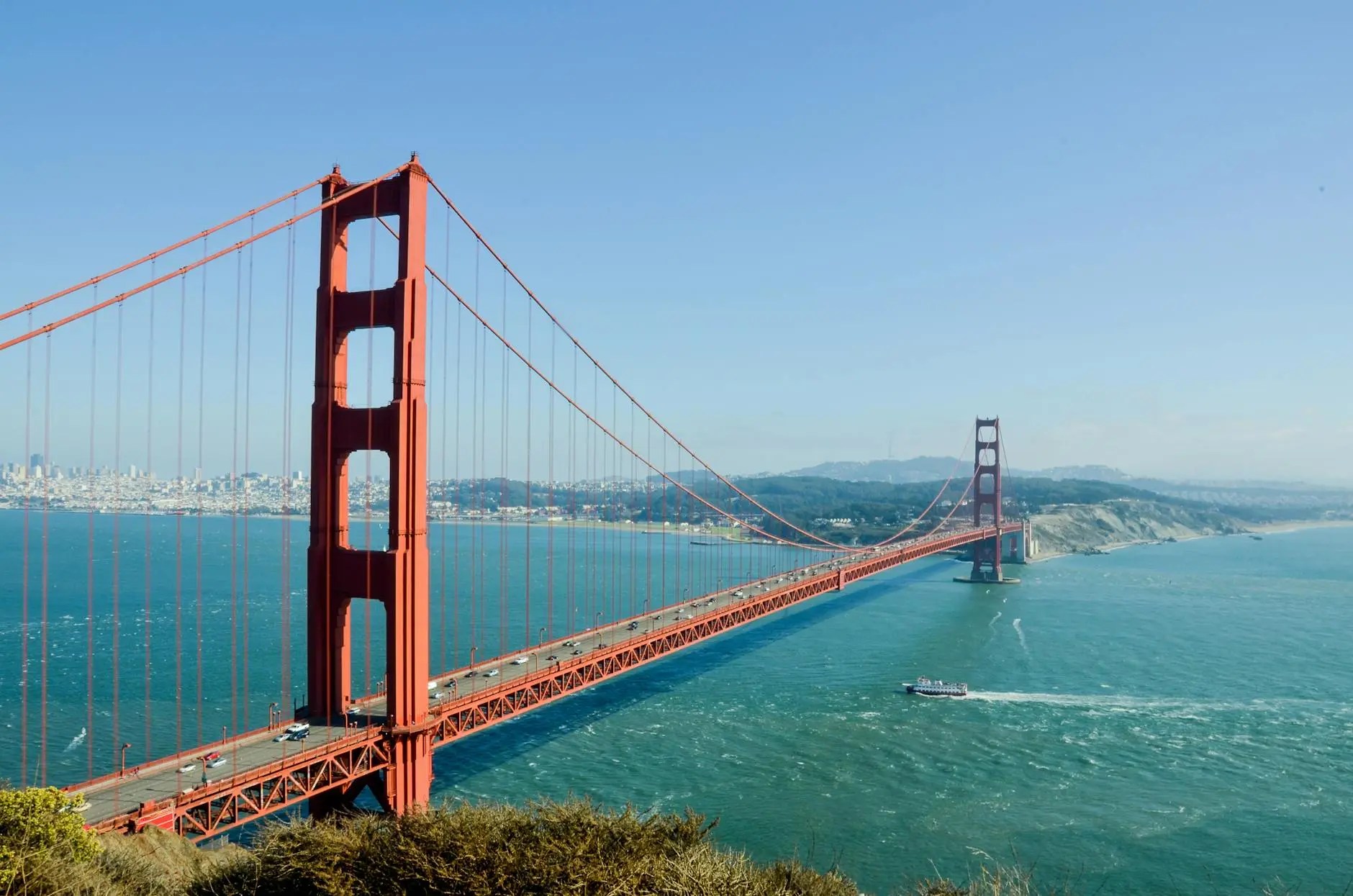 The Golden Gate Bridge spans over the blue waters of the San Francisco Bay on a clear day, showcasing its iconic red-orange color.