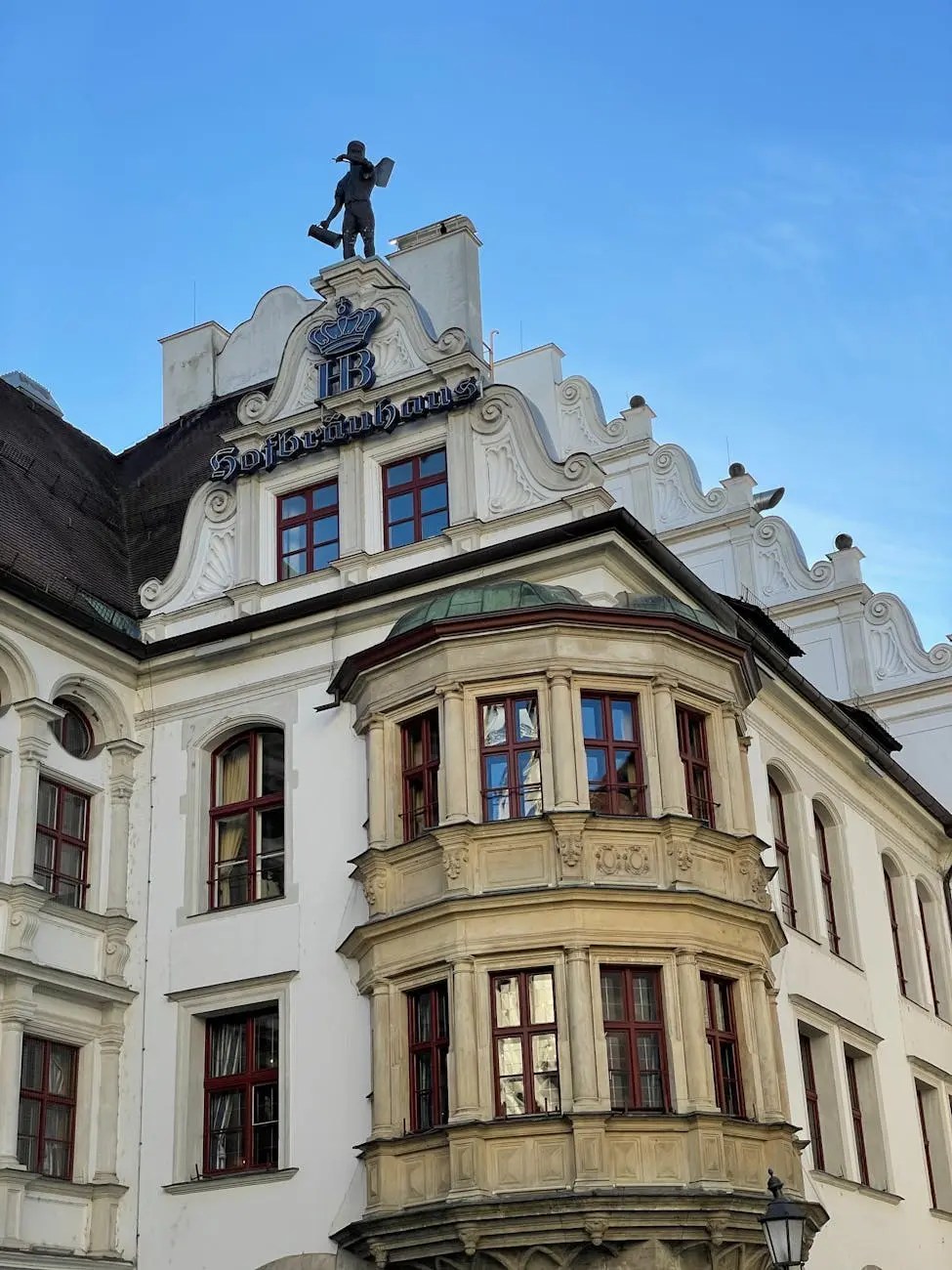 View of the Hofbräuhaus building in Munich, featuring ornate architecture and a statue of a beer carrier on the roof.