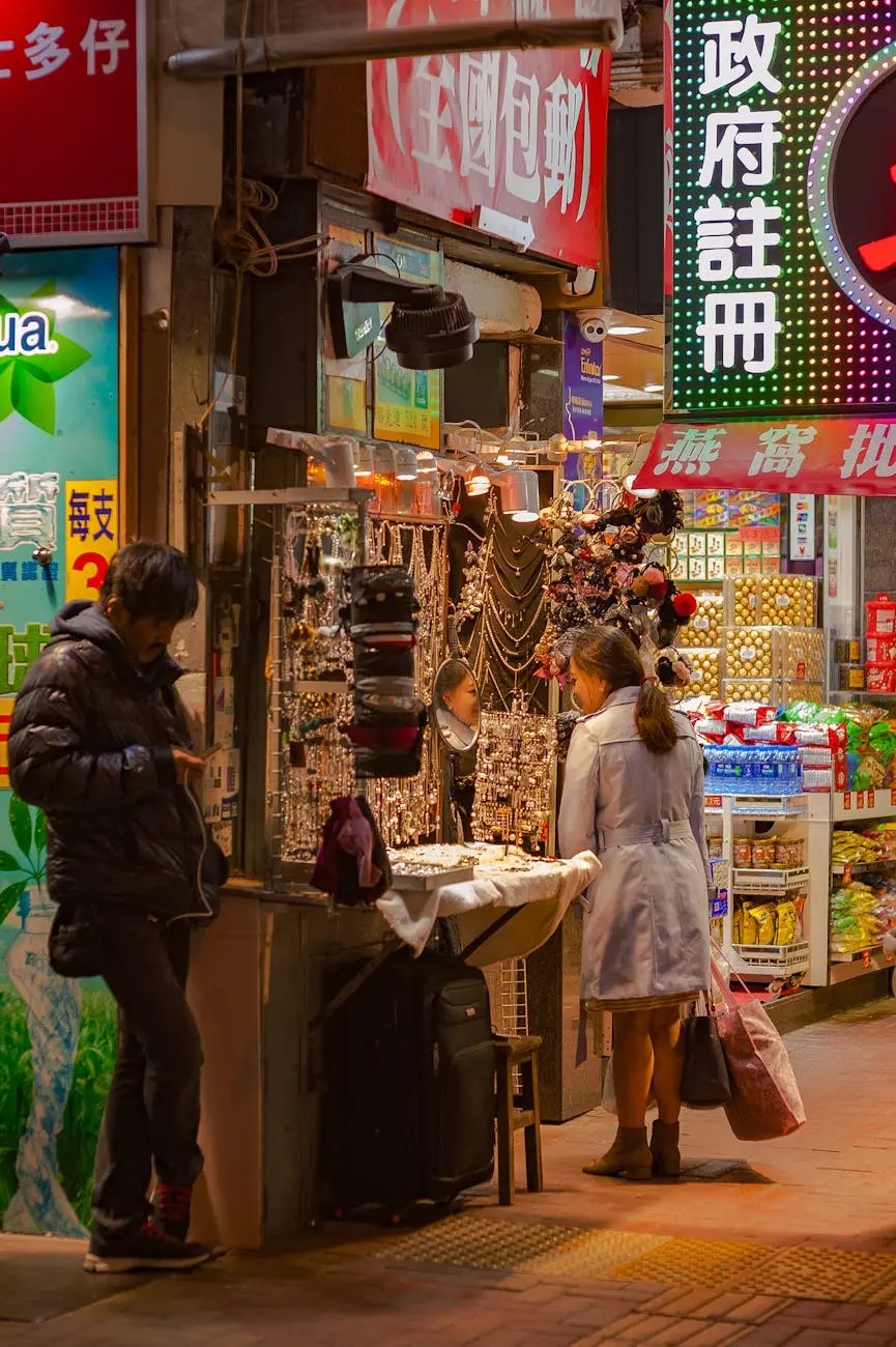 A nighttime market scene in Hong Kong showcasing a vendor selling jewelry and accessories, with a woman examining the merchandise while a man stands nearby looking at a phone.