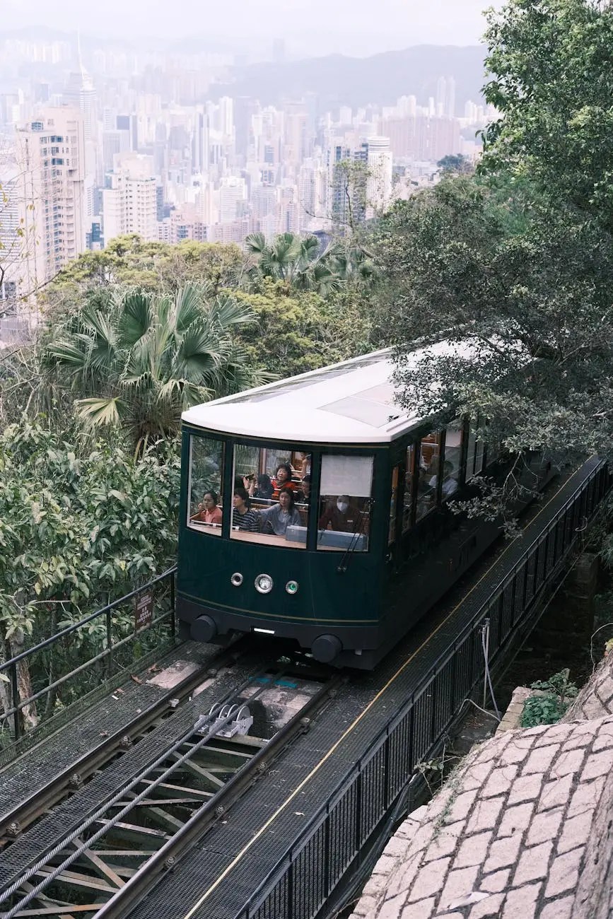 A vintage-style funicular train traveling up a steep incline surrounded by lush greenery, with a view of a city skyline in the background.