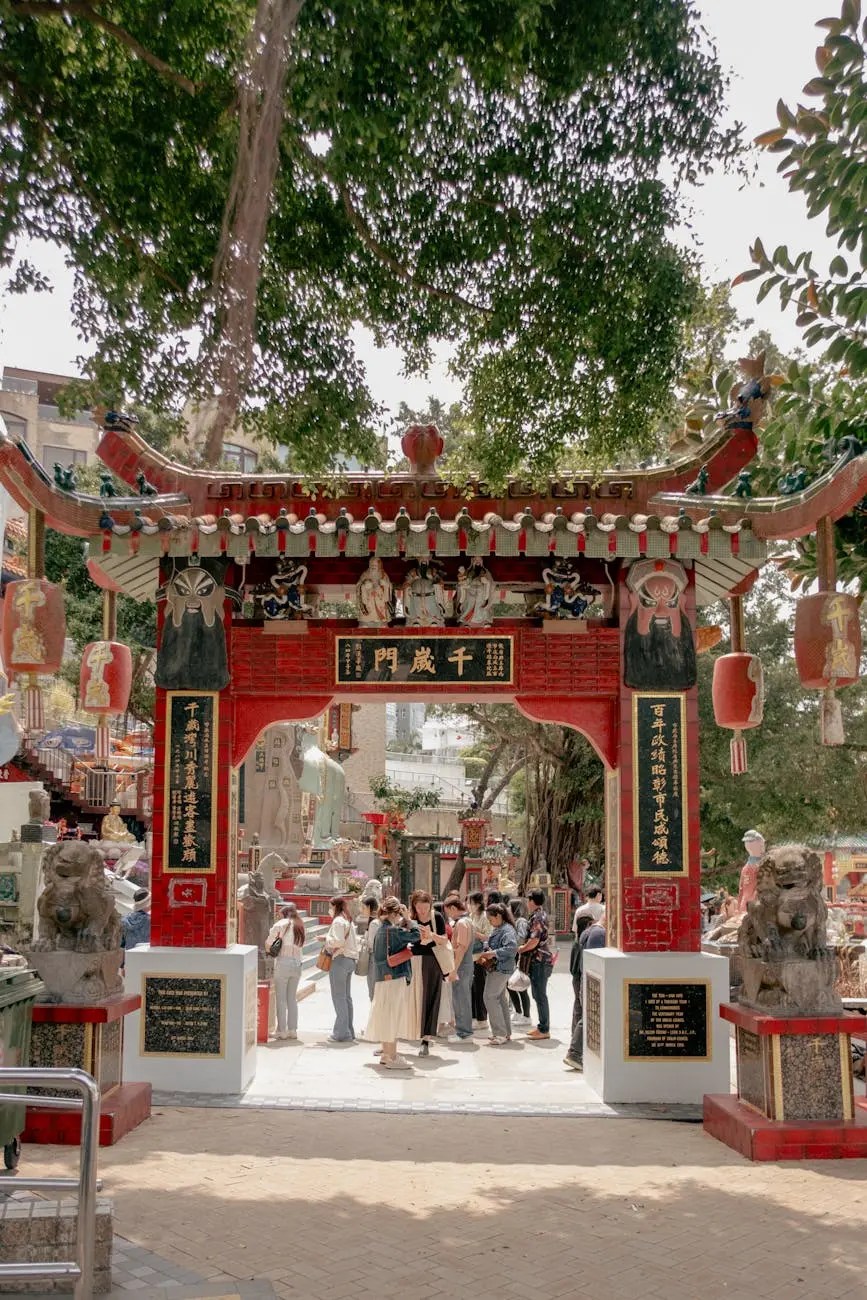 A traditional Chinese temple gate with intricate designs and decorations, surrounded by greenery, with a group of people gathering at the entrance in Hong Kong.