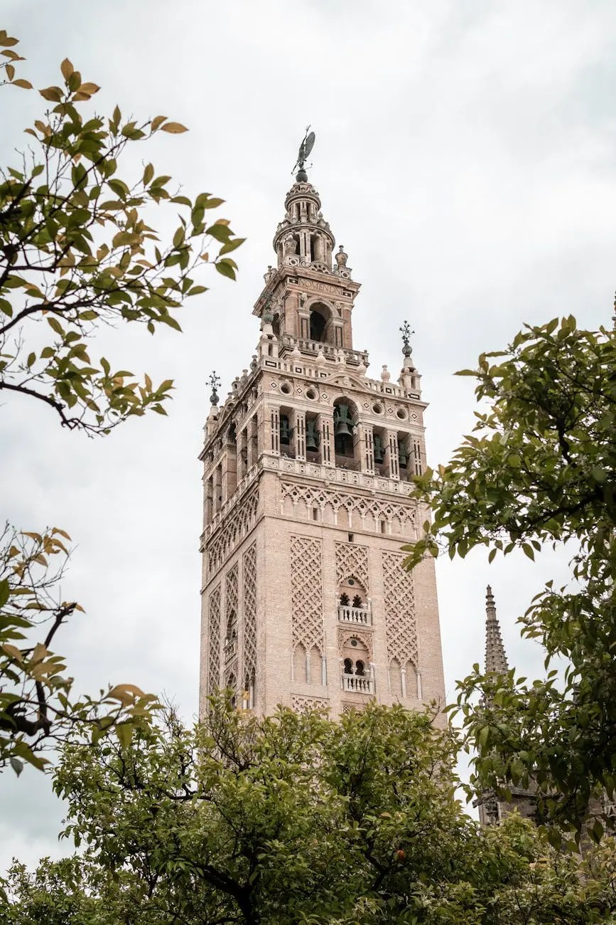 Close-up view of La Giralda tower in Seville, Spain, framed by green leaves and a cloudy sky.