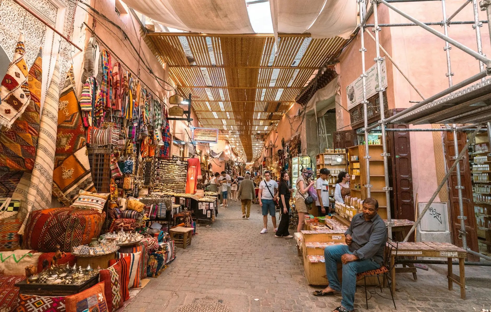 A vibrant souk in Marrakech, filled with colorful textiles, spices, and artisan goods, showcasing a lively atmosphere with shoppers and vendors.
