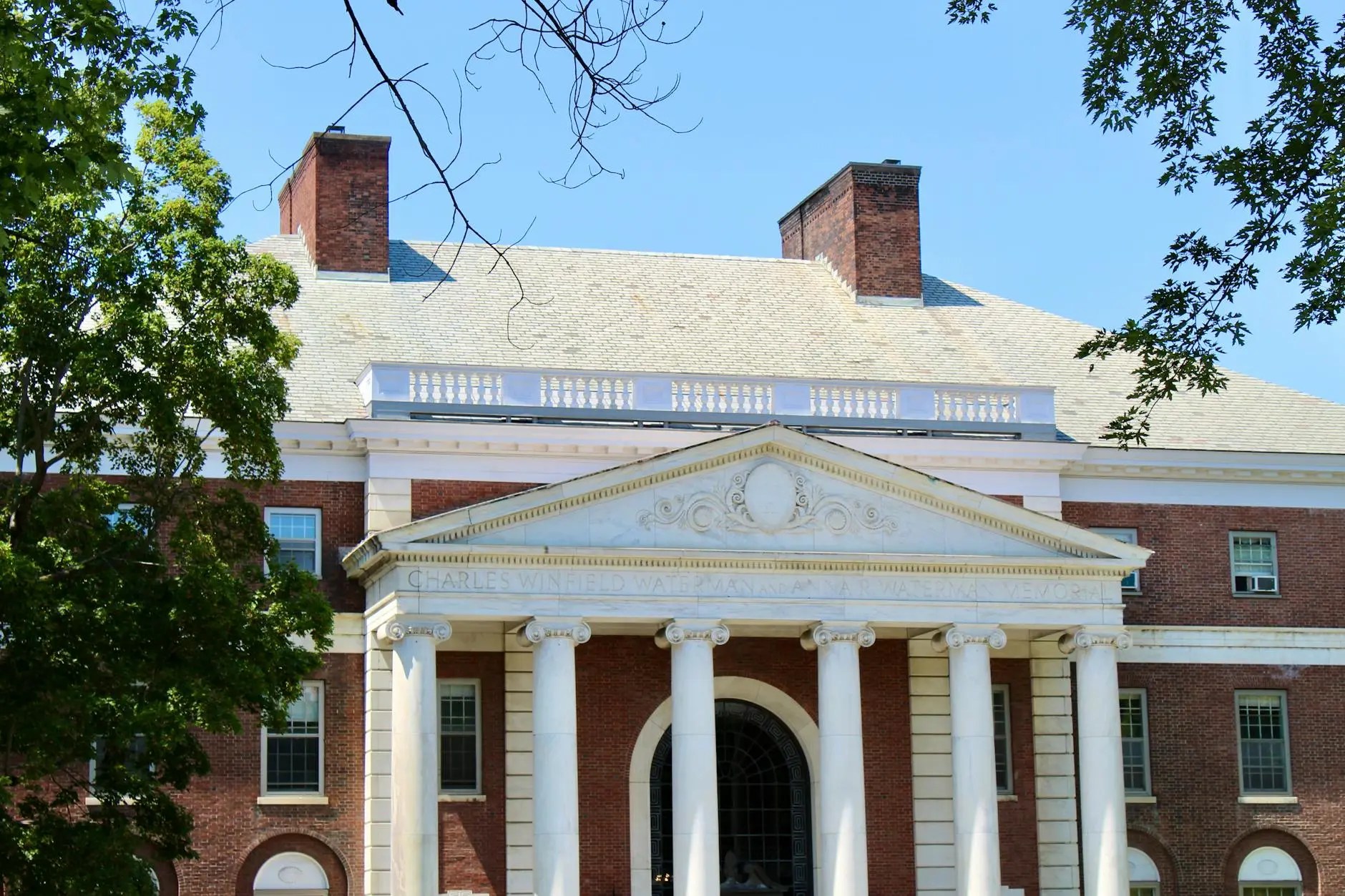 Facade of a historic building featuring grand columns and intricate architectural details, surrounded by green trees against a clear blue sky.