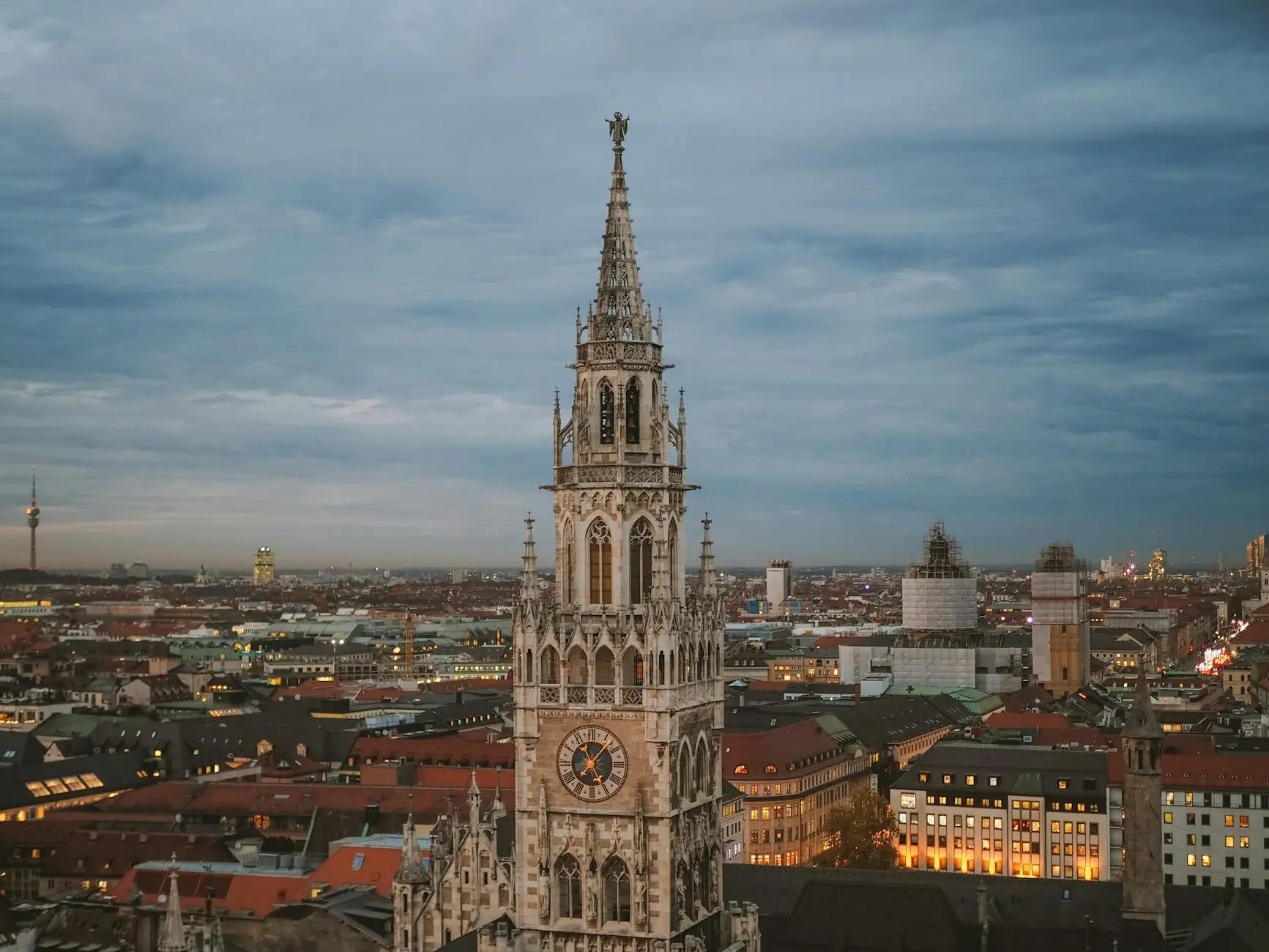 Panoramic view of Munich featuring the ornate architecture of the city hall with its spire against a twilight sky.