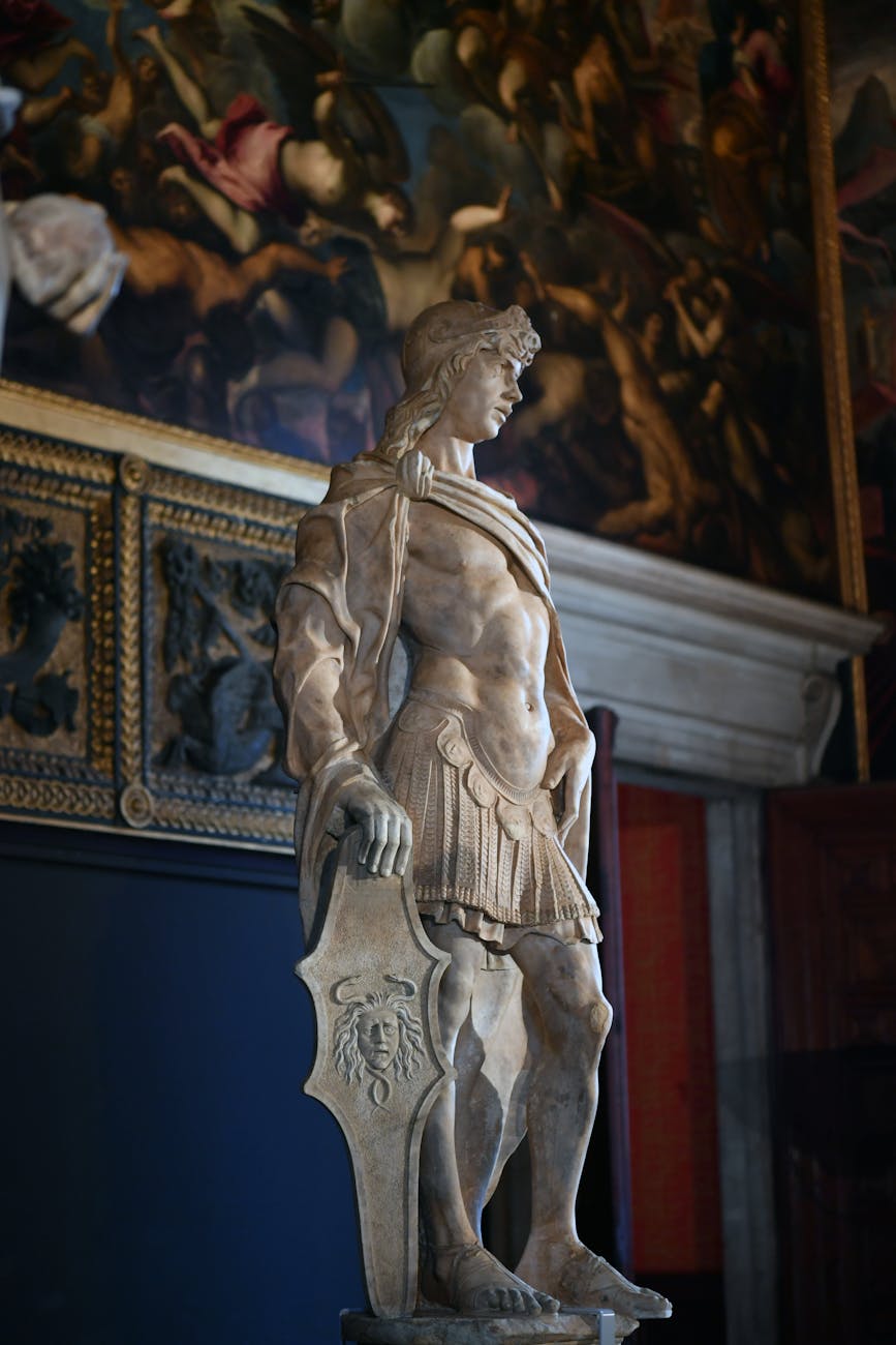 A marble statue of a warrior holding a shield, set against a richly decorated backdrop featuring historical paintings.