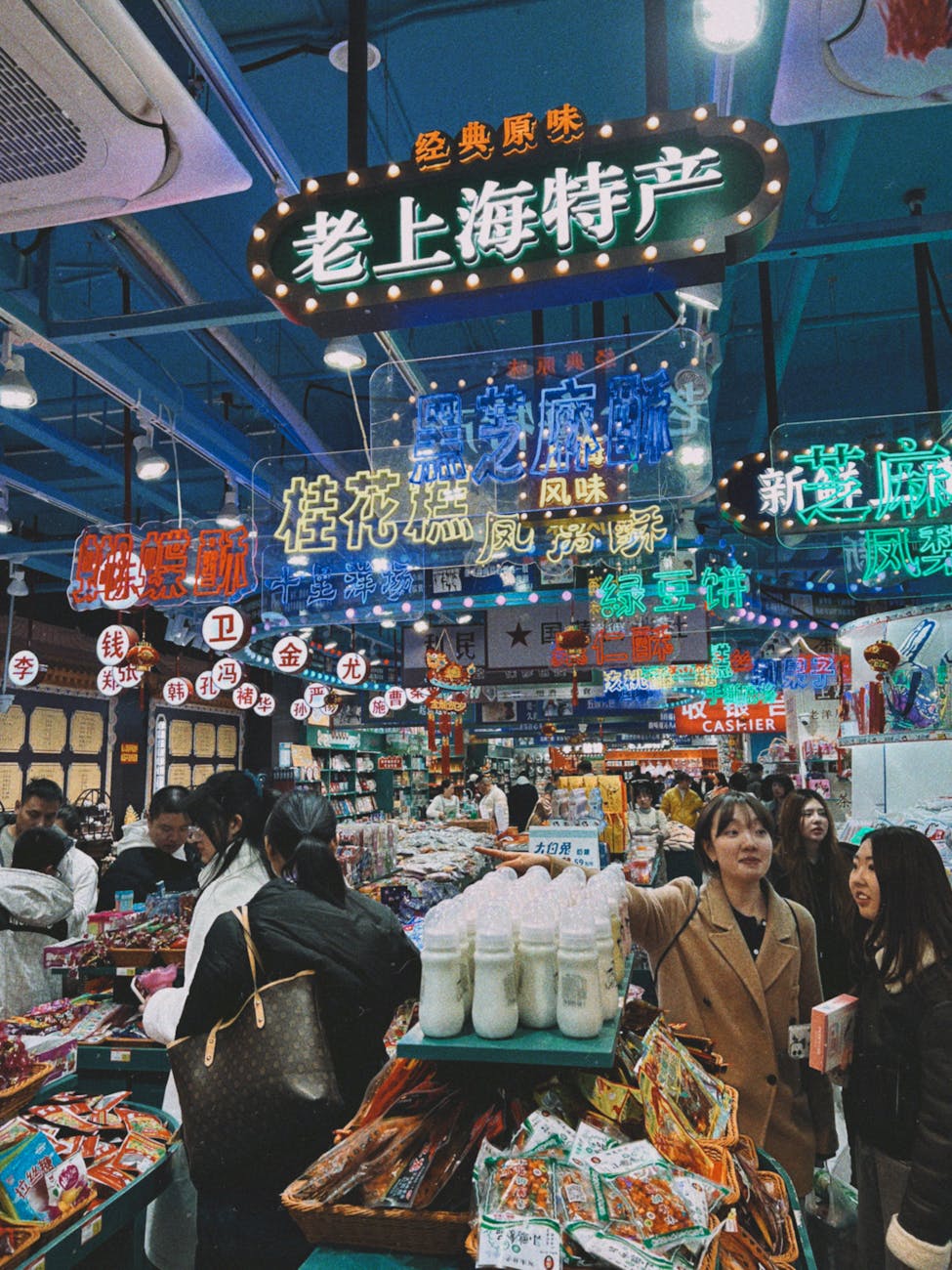 A busy market scene in Shanghai filled with colorful neon signs and a variety of food products, where people are browsing and shopping.