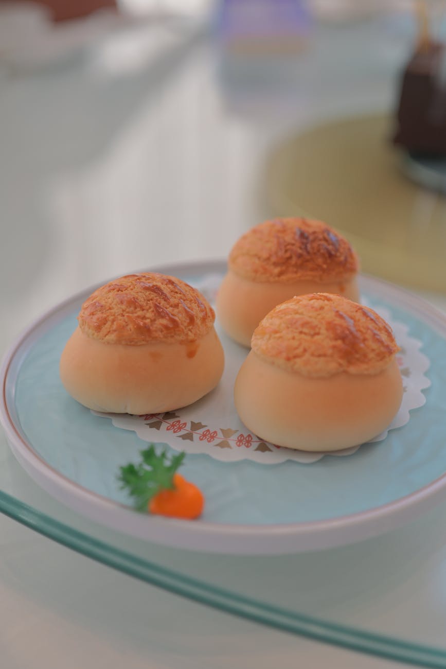 Three golden-brown baked buns on a pale blue plate, garnished with a small carrot and parsley.