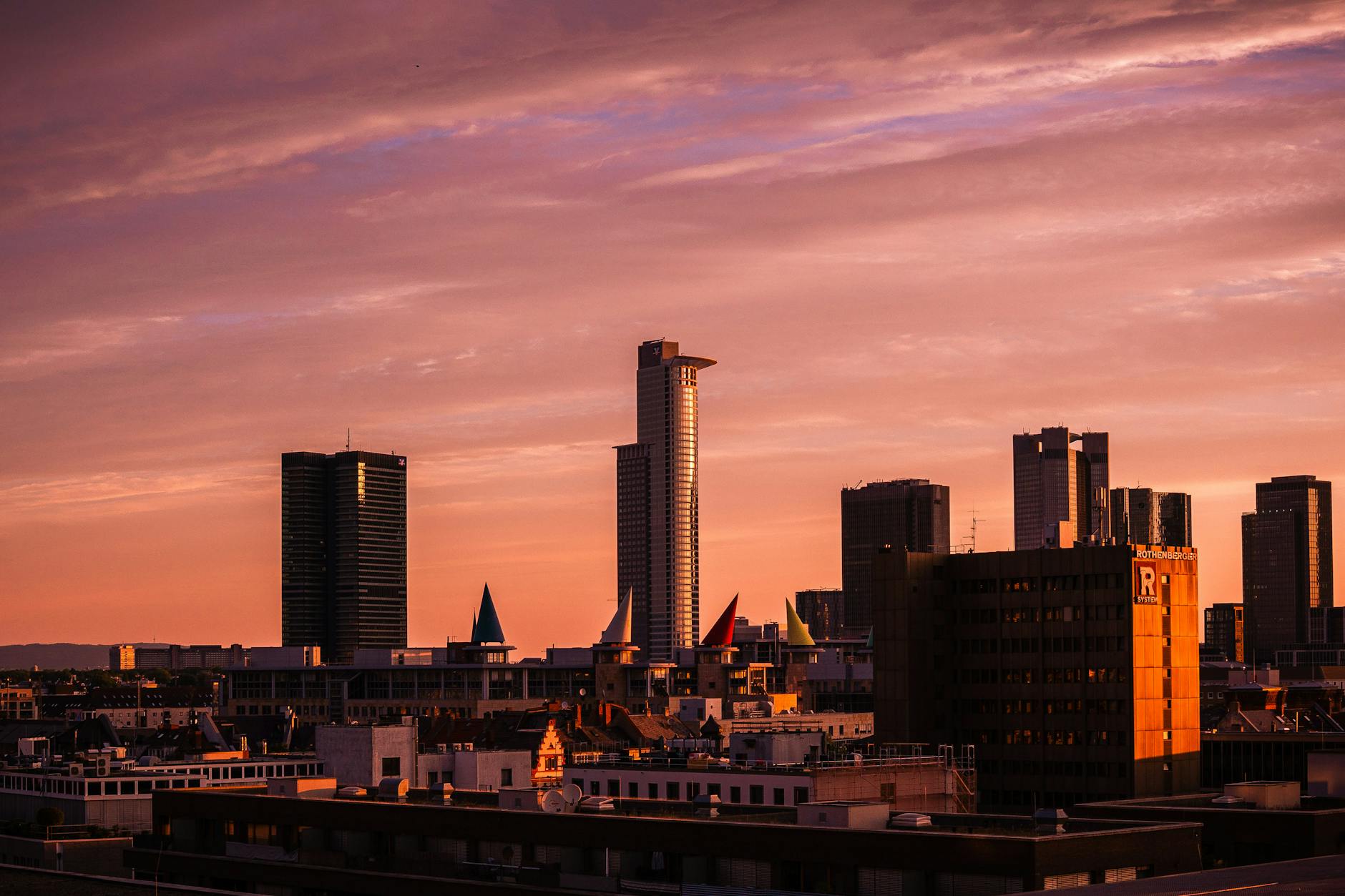 Skyline of Frankfurt am Main at sunset, featuring modern skyscrapers and colorful rooftops against a vibrant sky.