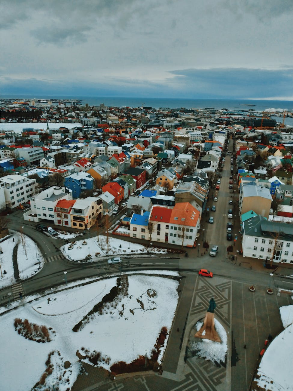 Aerial view of Reykjavik, Iceland, showcasing colorful rooftops, snow-covered streets, and a coastal backdrop under a cloudy sky.